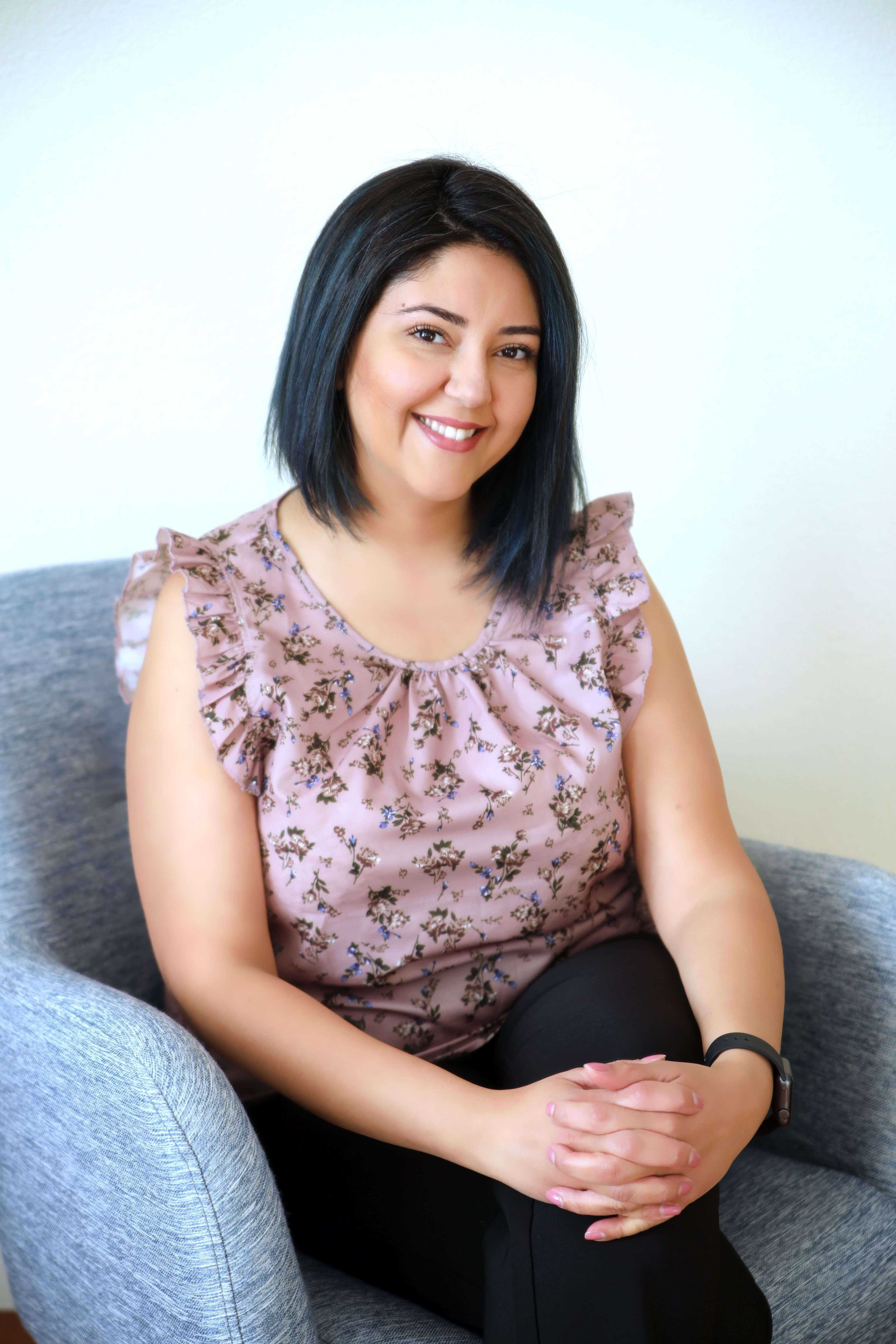 Doctor Khoramshahi, Brunette woman, sitting and smiling in a beige top and dark pants